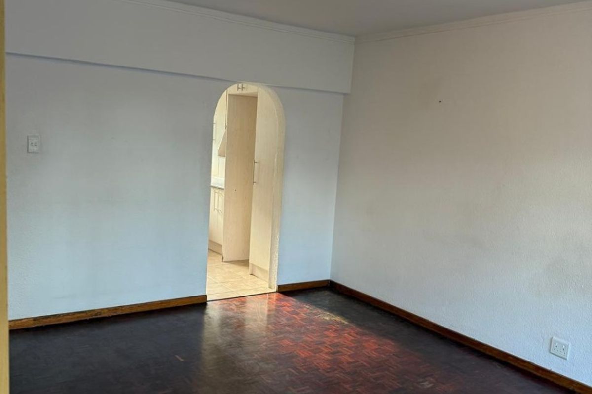 An empty living room featuring dark parquet flooring and a distinctive arched doorway leading to the kitchen area.