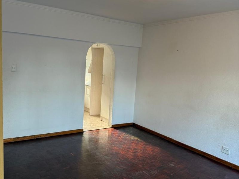 An empty living room featuring dark parquet flooring and a distinctive arched doorway leading to the kitchen area.