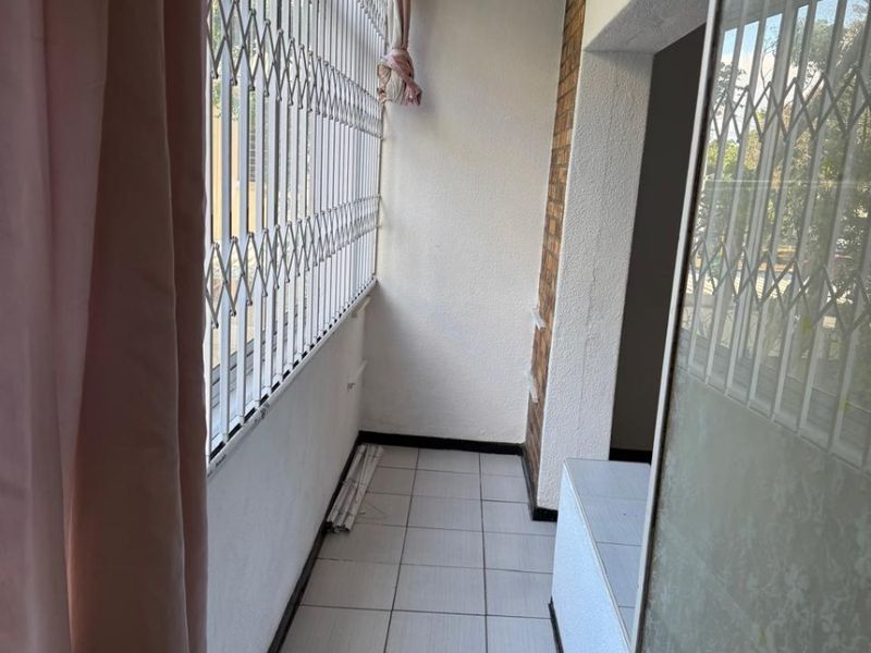 A narrow, enclosed balcony featuring tiled flooring, a brick feature wall, and security gates, offering a functional outdoor space.