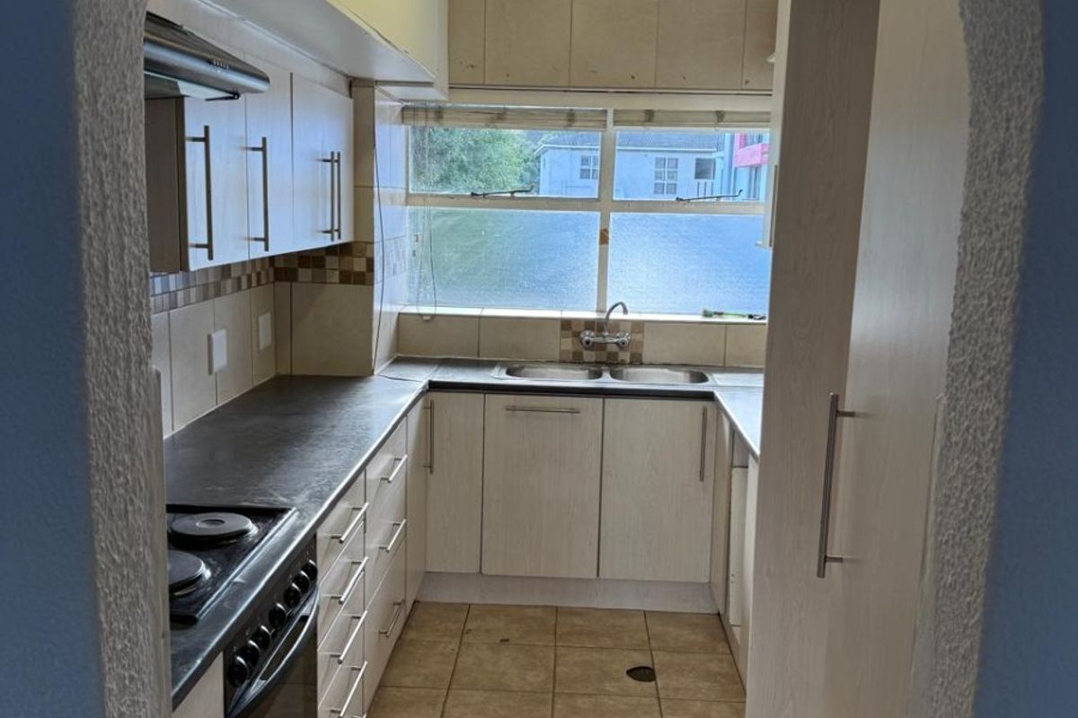 A functional galley-style kitchen featuring built-in cabinetry, a double sink, and an integrated electric stove with an extractor fan.