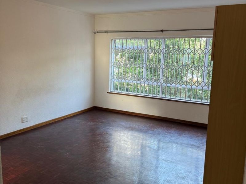 An empty bedroom featuring classic parquet flooring, a built-in cupboard, and a window fitted with a security gate.
