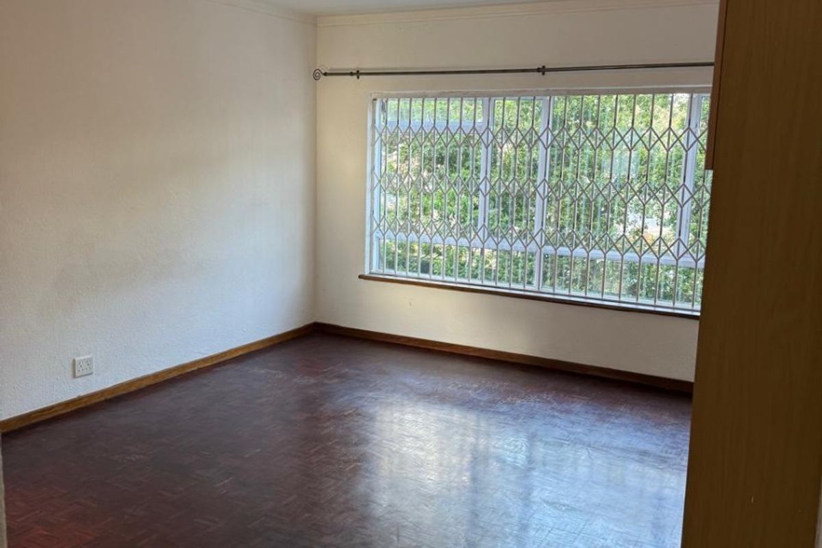 An empty bedroom featuring classic parquet flooring, a built-in cupboard, and a window fitted with a security gate.