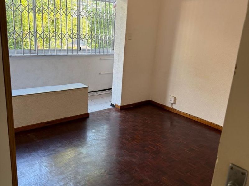 An empty bedroom featuring dark parquet flooring, a built-in bench, and a security gate leading to an adjacent balcony area.