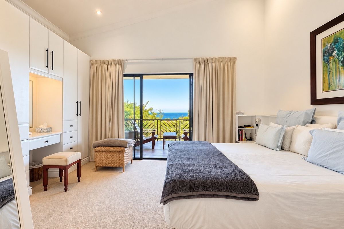 Spacious bedroom featuring built-in cabinetry, a vanity station, and sliding glass doors opening to a private balcony with scenic ocean views.