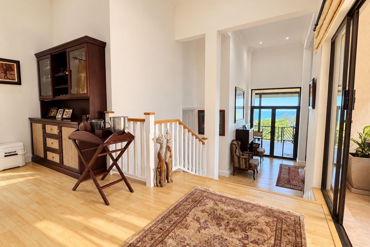 Spacious living area featuring light wood flooring, a classic staircase with balustrade, and large sliding glass doors leading to an outdoor balcony with ocean views.