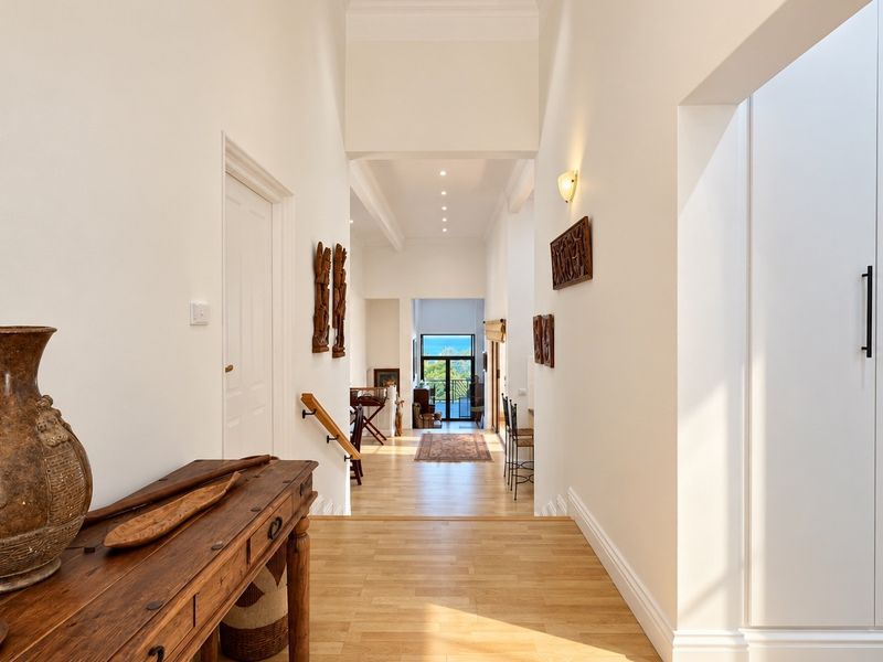 A bright and spacious hallway featuring high ceilings, light wood flooring, and built-in storage cabinetry, leading towards an open living area with a view.