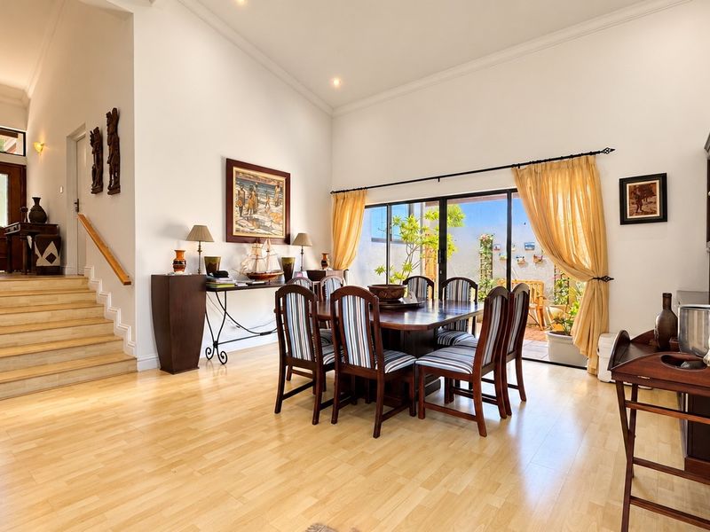 Spacious dining area featuring light timber flooring, high ceilings with recessed lighting, and large sliding glass doors providing access to the outdoor patio.