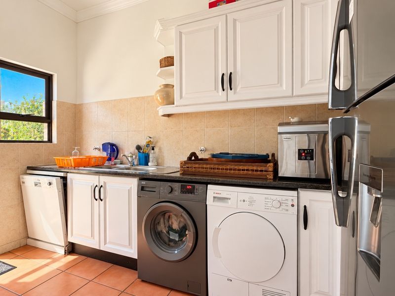 A functional laundry room featuring built-in cabinetry, tiled backsplash, stainless steel sink, and integrated laundry appliances with direct access to an outdoor patio area.