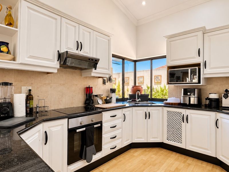 A well-maintained kitchen featuring white cabinetry, granite countertops, a corner sink, and integrated appliances including an oven, hob, and microwave.