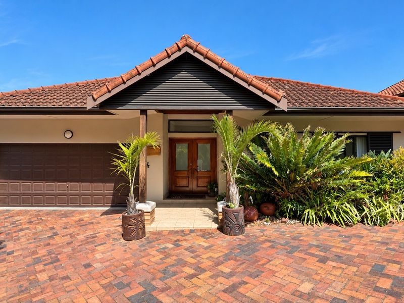 Front elevation of a well-maintained house featuring a tiled roof, double garage, and a welcoming timber entrance door with a paved driveway.