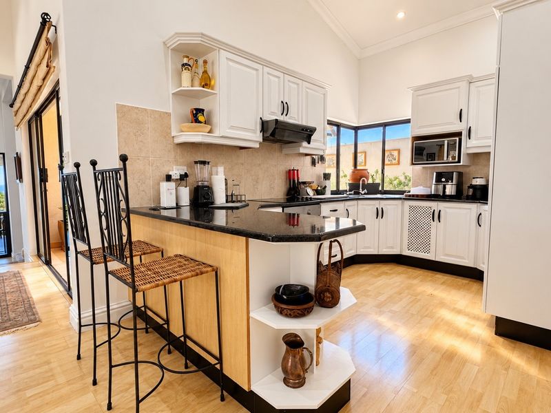 A well-lit kitchen featuring white cabinetry, granite countertops, a breakfast bar, and integrated appliances, with direct access to an outdoor balcony area.