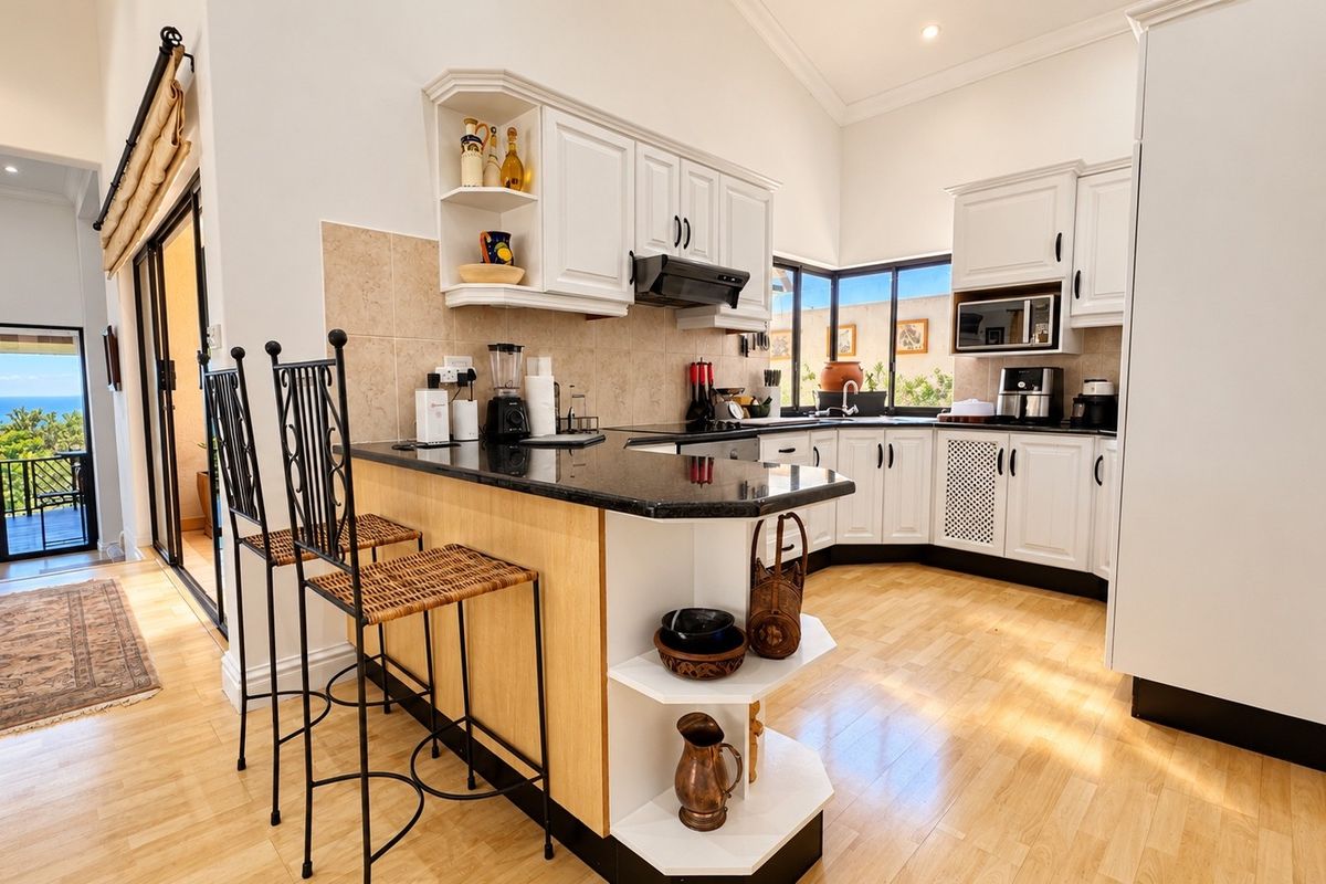 A well-lit kitchen featuring white cabinetry, granite countertops, a breakfast bar, and integrated appliances, with direct access to an outdoor balcony area.