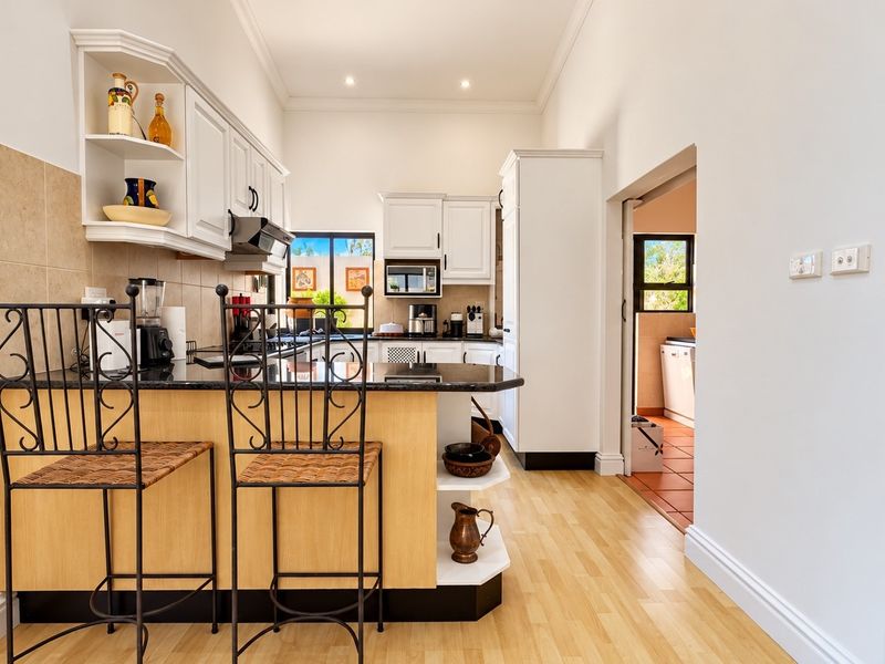 A well-maintained kitchen featuring white cabinetry, granite countertops, built-in appliances, and laminate flooring, with an adjacent utility area visible.