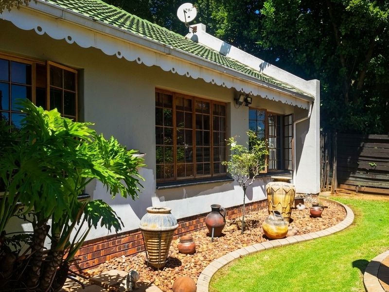A well-maintained rear exterior view featuring a tiled roof, decorative eaves, timber-framed windows, and a landscaped garden with stone pathways and brick edging.
