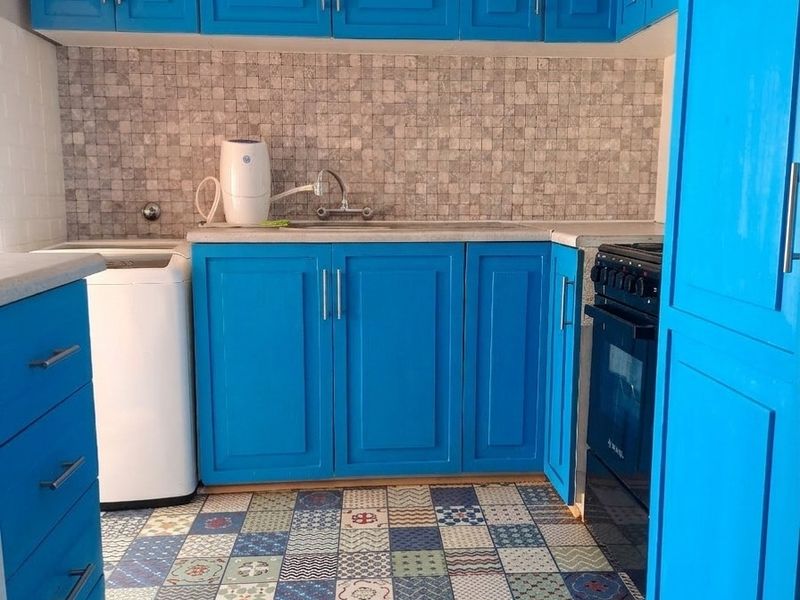 A vibrant kitchen featuring bright blue cabinetry, a mosaic tile backsplash, and decorative patterned floor tiles with integrated stove and sink.