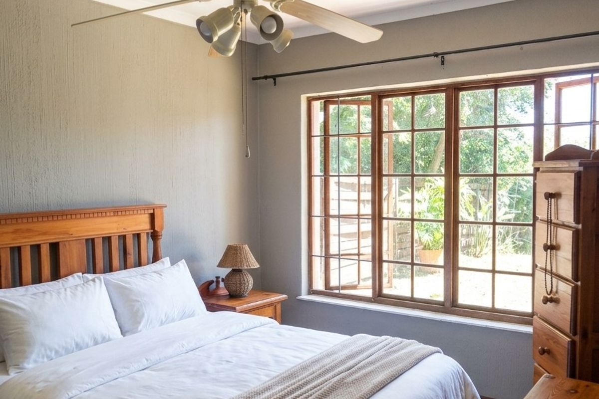 A cozy bedroom featuring a ceiling fan and large timber-framed windows that provide natural light and views of the garden.