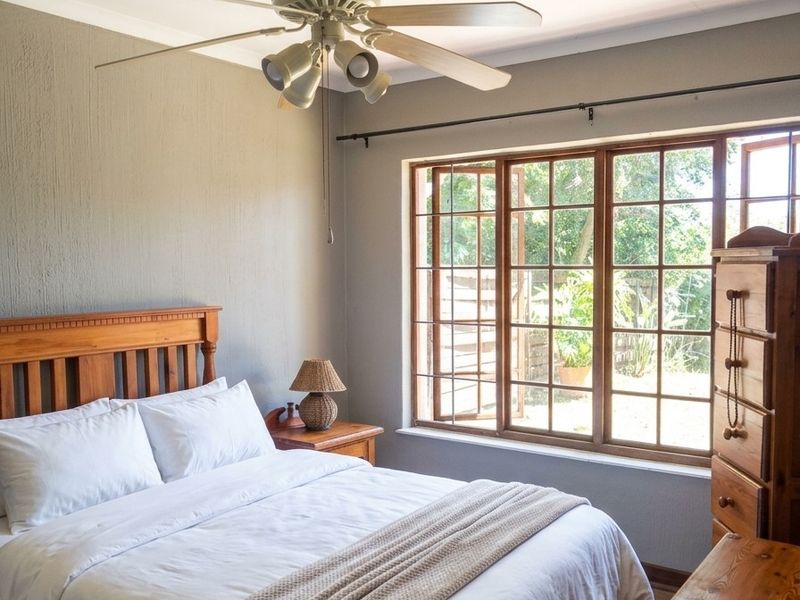 A cozy bedroom featuring a ceiling fan and large timber-framed windows that provide natural light and views of the garden.