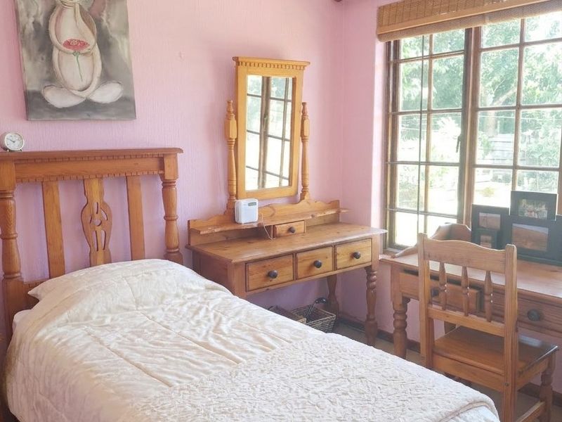 A cozy bedroom featuring a timber-framed window, neutral carpeting, and pink wall finishes, offering a comfortable and functional living space.