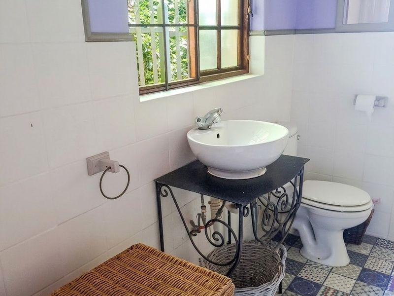A compact bathroom featuring a vessel sink on a metal vanity, patterned floor tiles, and white wall tiling.