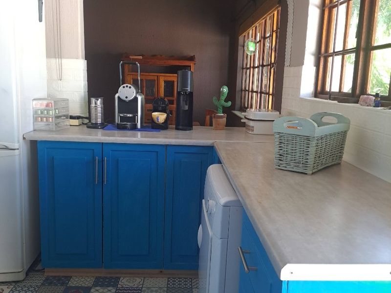 A functional kitchen featuring blue cabinetry, laminate countertops, and patterned floor tiles, with a pass-through window connecting to the adjacent living space.