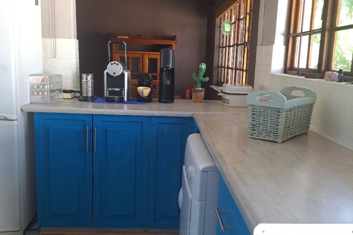 A functional kitchen featuring blue cabinetry, laminate countertops, and patterned floor tiles, with a pass-through window connecting to the adjacent living space.