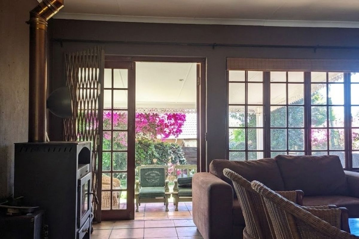 Living room featuring a freestanding fireplace with flue, tiled flooring, and large multi-pane windows and doors providing access to the garden.