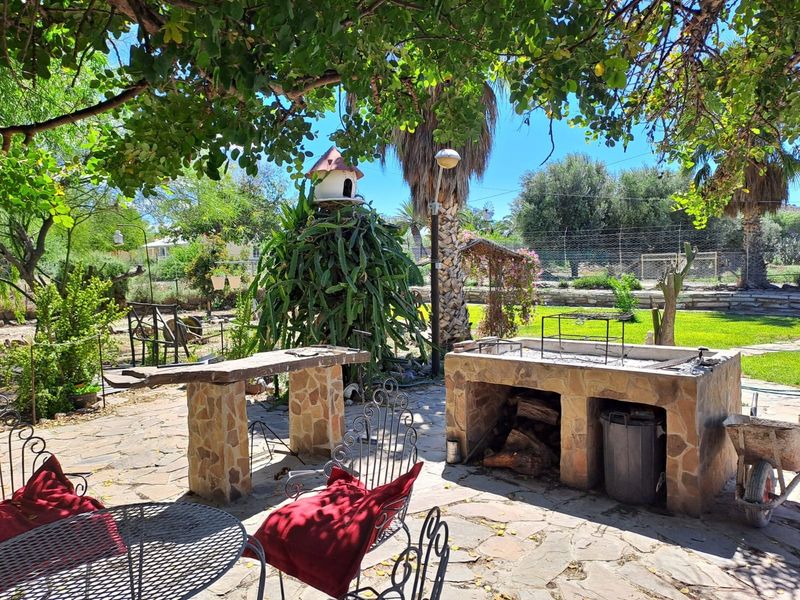 Outdoor entertainment area featuring a stone-clad built-in braai, matching prep counter, and flagstone paving set within a landscaped garden.