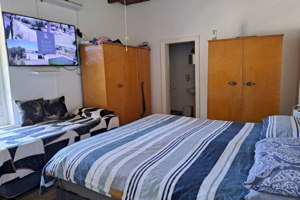 A bedroom featuring exposed timber ceiling beams, built-in wooden cupboards, and an en-suite bathroom entrance, providing a functional layout with potential for modernization.