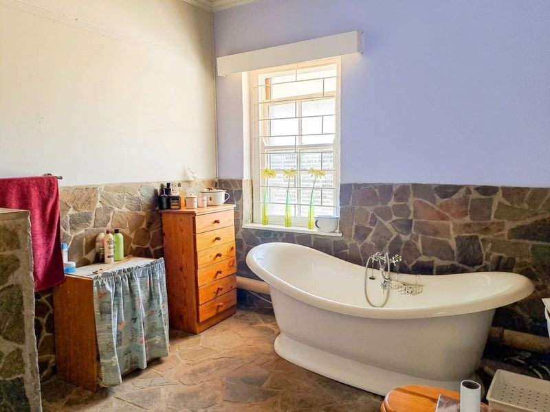 Bathroom featuring a freestanding bathtub, stone wall cladding, and stone flooring, offering a rustic aesthetic with potential for modern updates.