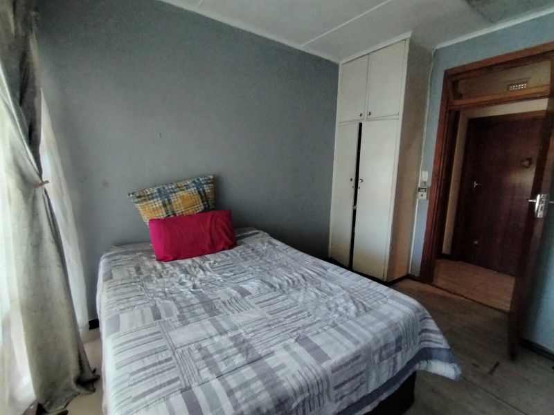 A bedroom featuring a built-in cupboard and wooden door frame, requiring cosmetic updates to the wall finishes and general maintenance.