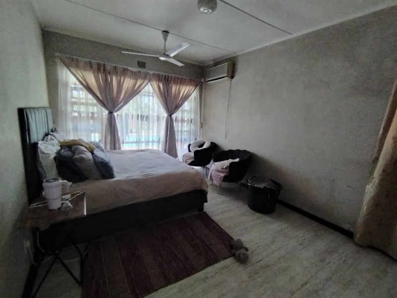 A bedroom featuring tiled flooring, a ceiling fan, and a wall-mounted air conditioning unit, with visible wear on the wall finishes.