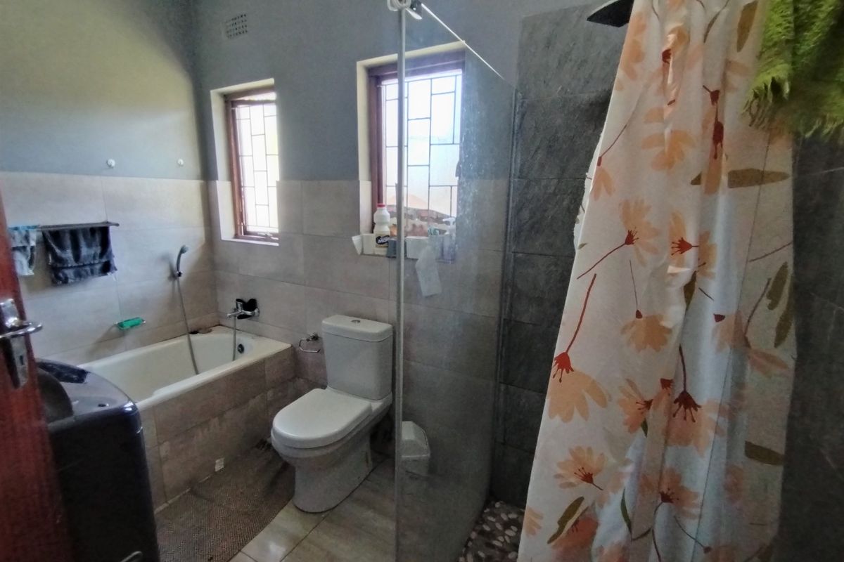 A functional bathroom featuring a built-in bathtub, a separate shower with a glass screen, and neutral wall and floor tiling.