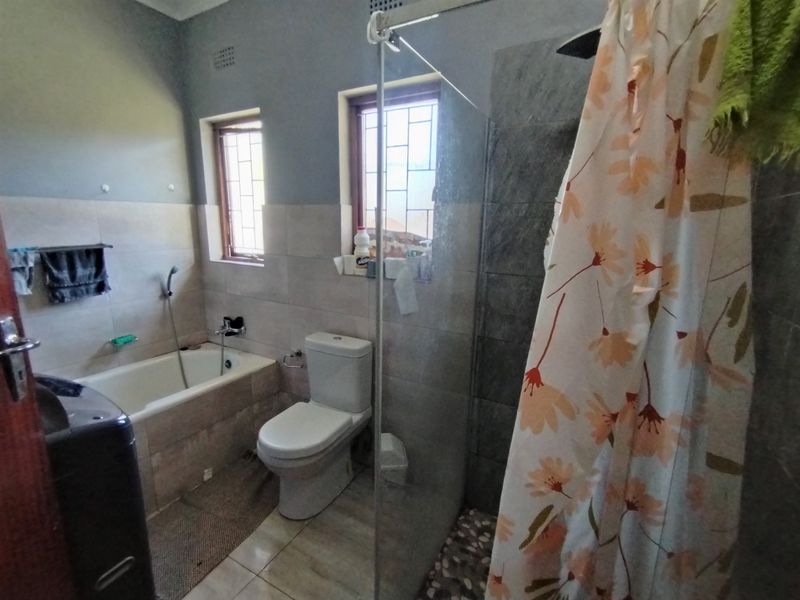 A functional bathroom featuring a built-in bathtub, a separate shower with a glass screen, and neutral wall and floor tiling.