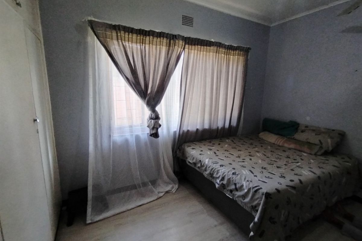 A bedroom featuring laminate flooring and a built-in cupboard, requiring cosmetic updates to the wall finishes and ceiling.