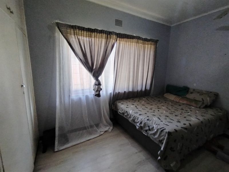 A bedroom featuring laminate flooring and a built-in cupboard, requiring cosmetic updates to the wall finishes and ceiling.