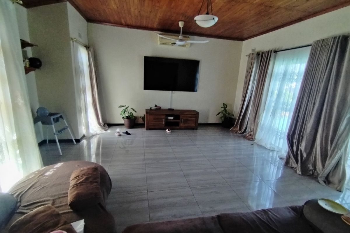 Spacious living room featuring a warm timber tongue and groove ceiling, large format floor tiles, and sliding glass doors providing ample natural light.