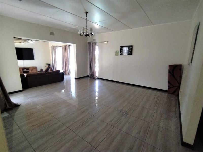 Spacious open-plan living area featuring large format floor tiles, neutral walls, and a classic chandelier, offering a versatile layout for dining and lounge arrangements.