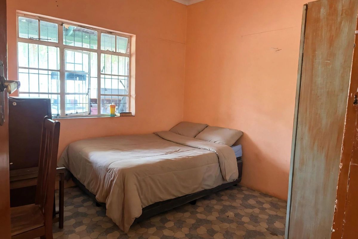 A bedroom featuring tiled flooring and security bars on the window, currently finished with peach-toned wall paint.