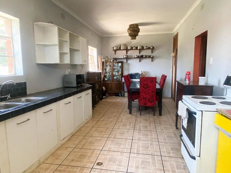 Open-plan kitchen and dining area featuring tiled flooring, built-in cabinetry, and a double basin sink, offering a functional space with potential for modern updates.