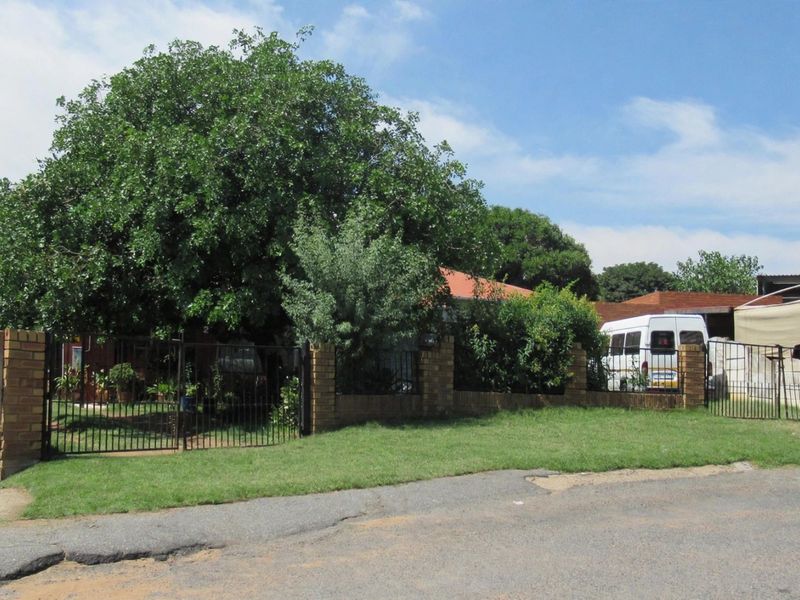 Front view of the property featuring a brick boundary wall, metal security gate, and a well-maintained lawn area.