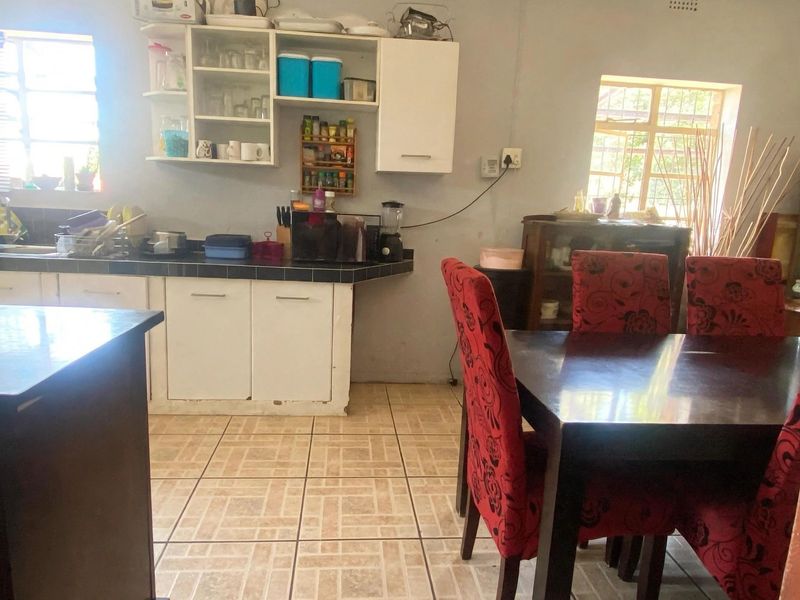Open plan kitchen and dining area featuring tiled flooring, built-in cabinetry with tiled countertops, and natural light from multiple windows.