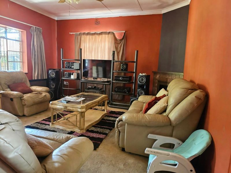 A living room featuring a fireplace, ceiling fan, and coving, currently finished with dated wall paint and worn carpeting.