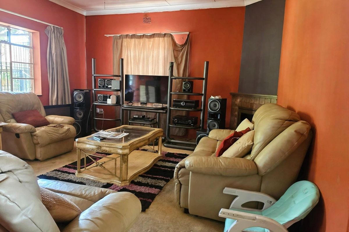 A living room featuring a fireplace, ceiling fan, and coving, currently finished with dated wall paint and worn carpeting.
