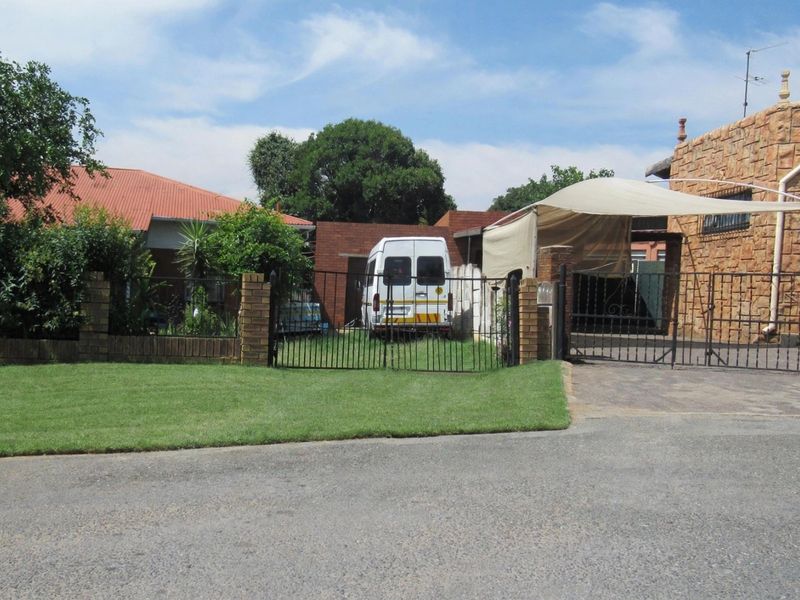 Front view of the property featuring a paved driveway, carport, brick boundary wall, and wrought iron gate entrance.