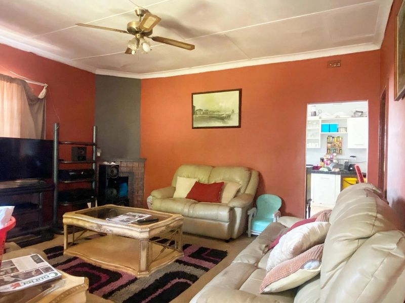 A living room featuring a brick fireplace, ceiling fan, and coved ceiling, with an adjacent view into a kitchen area.