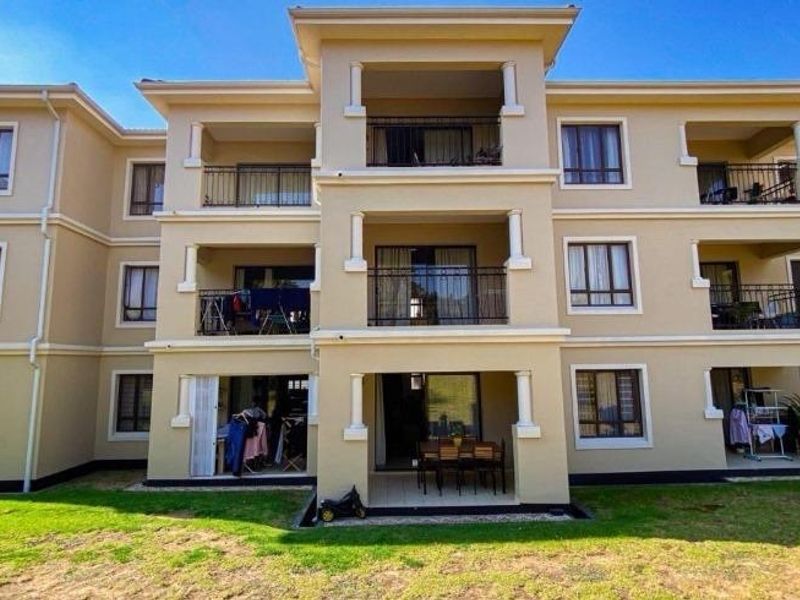 Rear elevation of a multi-story residential building featuring multiple balconies with metal railings and ground-floor patio access.