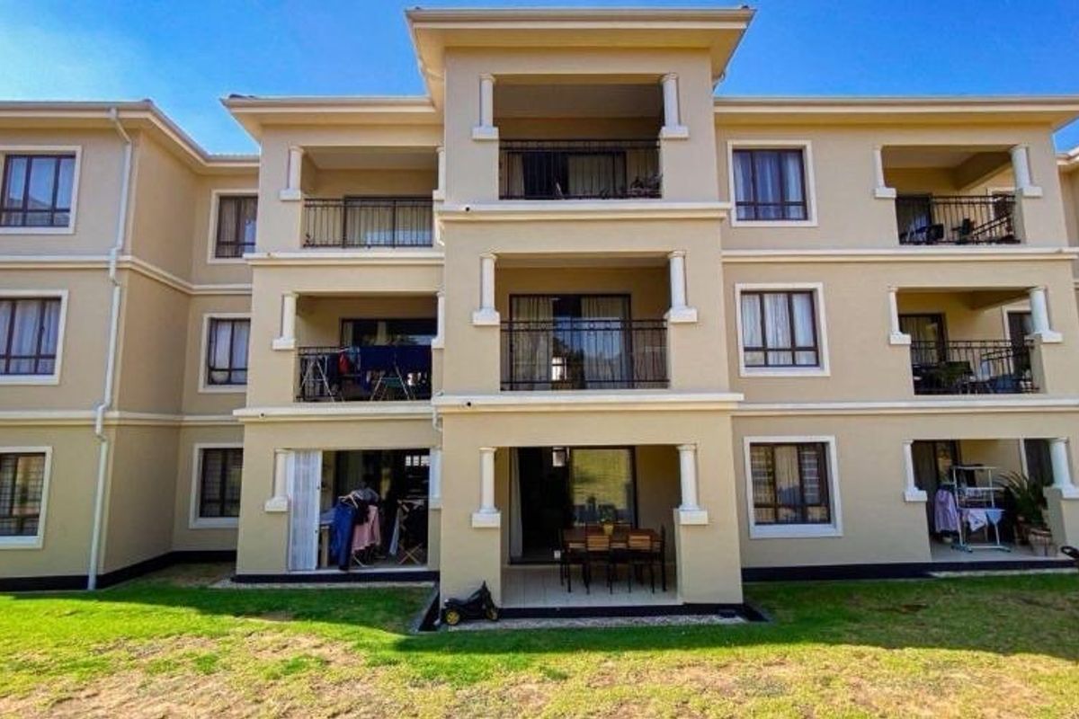 Rear elevation of a multi-story residential building featuring multiple balconies with metal railings and ground-floor patio access.