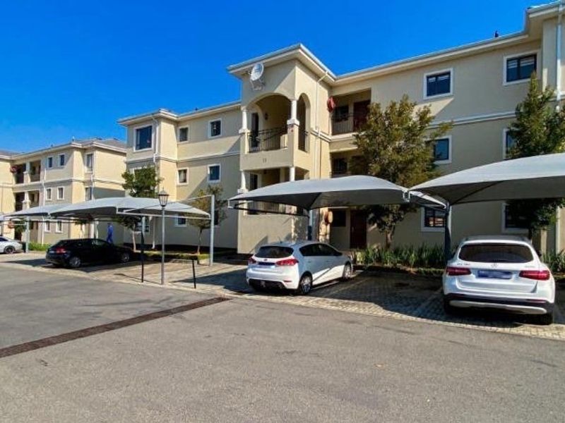 Exterior view of a multi-story residential apartment complex featuring covered parking bays and paved driveway access.