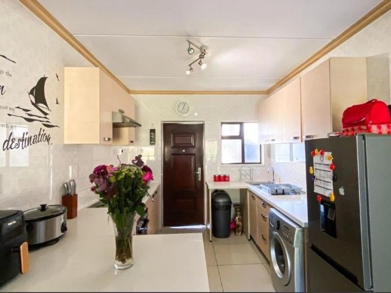 A functional galley-style kitchen featuring light-toned cabinetry, tiled splashbacks, and integrated laundry plumbing, providing a practical workspace with direct exterior access.