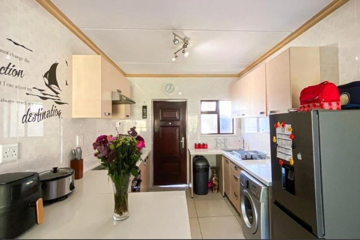 A functional galley-style kitchen featuring light-toned cabinetry, tiled splashbacks, and integrated laundry plumbing, providing a practical workspace with direct exterior access.